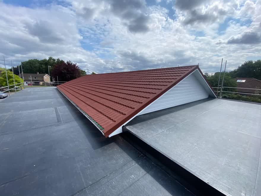 Red tiled hip roof meeting a newly laid grey flat roof below it