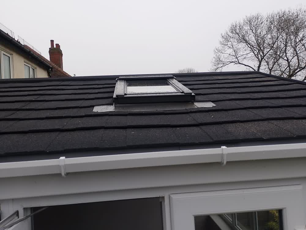Roof window set into a newly tiled dark roof above new guttering